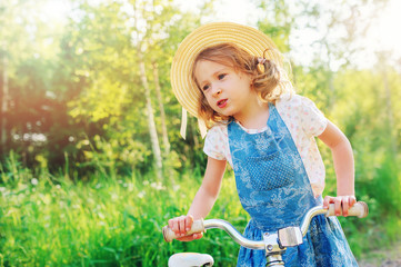 child girl with bicycle on country road, summer outdoor activities