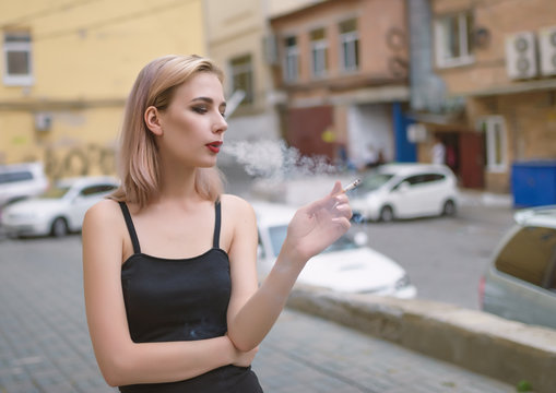 Beautiful girl smokes while waiting in the street.