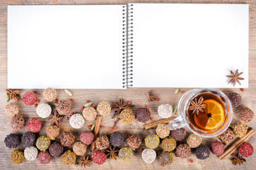 Handmade chocolate candies collection, dried oranges, cinnamon, cloves, cardamom, mulled wine, notebook on wooden background. Free space for your text.