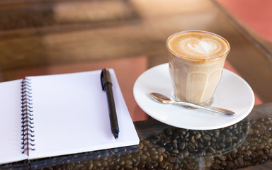 Hot latte art coffee cup on wooden table and note book, vintage