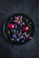 fresh dark fruits and berries on black background.
