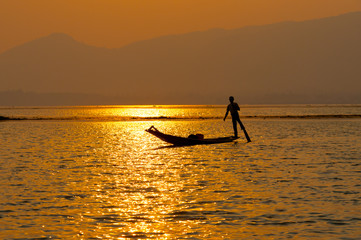 Fototapeta na wymiar INLE LAKE VILLAGE MYANMAR : Silhouette People rows the wooden boat by his leg in Inle Lake