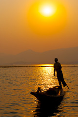 Fototapeta premium INLE LAKE VILLAGE MYANMAR : Silhouette People rows the wooden boat by his leg in Inle Lake