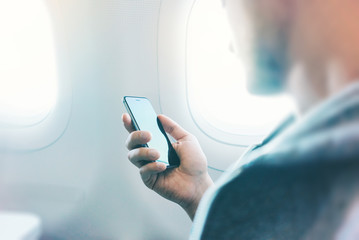 Closeup of businessman using modern smartphone in airplane 