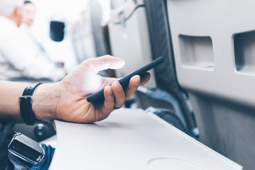 Closeup of male hand using smartphone at airplane