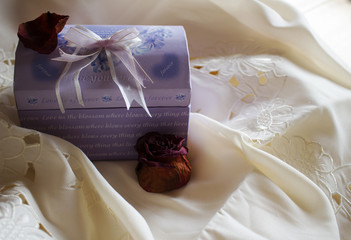 A lavender gift box with a red rose and a red petal

