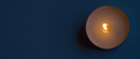 Single white candle on fire with free blue background space for your text.