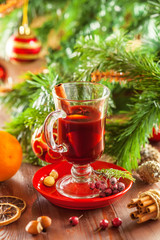 Glass of traditional hot drink on table by Christmas tree with decorations. Mulled wine.