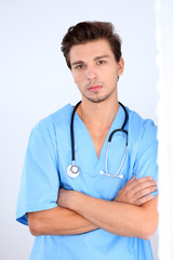 Attractive male doctor standing near the wall, crossed arms