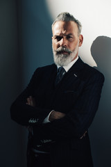 Portrait of bearded gentleman wearing trendy suit and stands against the wall