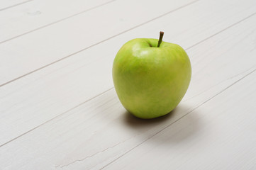 Green ripe apple on a white wooden surface