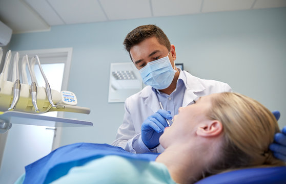 male dentist in mask checking female patient teeth