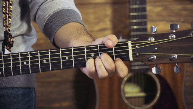 close up mans hand playing chords on acoustic guitar slow motion