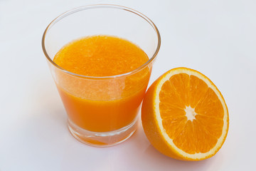 Glass of orange juice with half orange on white background