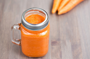 Healthy carrot smoothie in a jar with tube wooden background