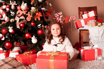 Obraz na płótnie Canvas Smiling kid girl 4-5 year old open christmas presents under christmas tree in room. Looking at camera. Childhood. 