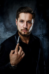 Elegant young handsome man. Studio fashion portrait.Man holding scissors and provocatively looking at camera