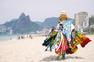 Beach vendor selling brightly colored kanga sarongs carries his merchandise along Ipanema Beach