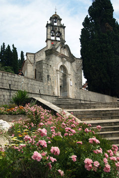 One of the 89 churches in Herceg Novi: Church of the Holy Savior on the Njegoseva street in the Topla area, vertical photo. Landscape with a baroque gate, flowers and an orthodox temple in Montenegro