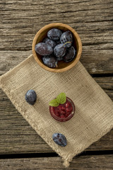 Top view of wooden bowl full of fresh ripe plums, a jar of home