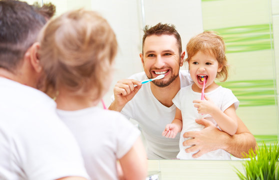 Happy family father and child girl brushing her teeth in bathroo
