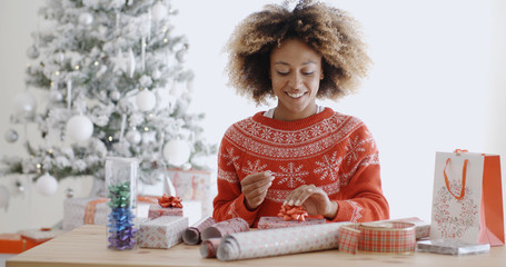 Happy young African woman wrapping presents - obrazy, fototapety, plakaty