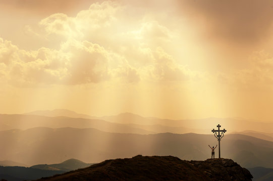 Man stands near the cross on top of mountain