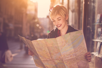 Young beautiful female traveler standing on the street and looking at the map