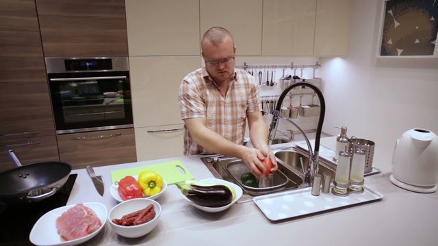 A man washing the vegetables in the kitchen sink