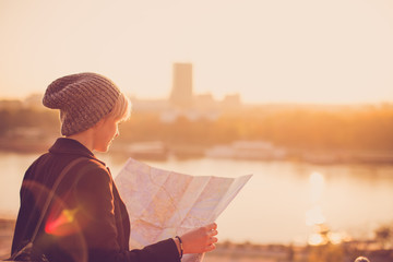Young female traveler standing in front of beautiful city view and looking at the map