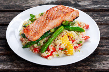 Fototapeta na wymiar Pan fried salmon with tender asparagus and courgette served on couscous mixed with sweet tomato, yellow pepper salsa.