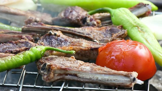 Ribs, green sweet pepper and tomato cooking on the grill over coals