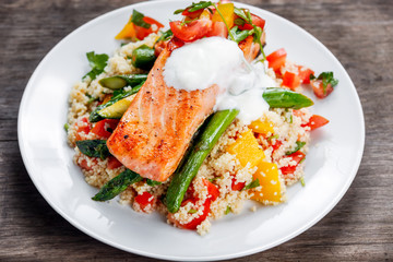 Pan fried Salmon with tender asparagus, courgette served on couscous mixed with sweet tomato, yellow pepper, with greek yogurt on old wooden table.