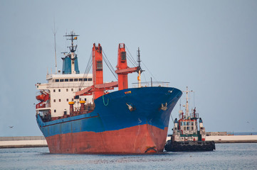 Naklejka premium Cargo ship and tug boat maneuvering near the pier