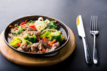 beef stew with vegetables in a frying pan over dark background