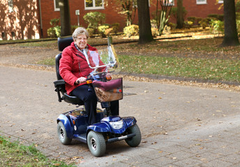 Seniorin mit Elektromobil fährt auf der Straße im Herbst