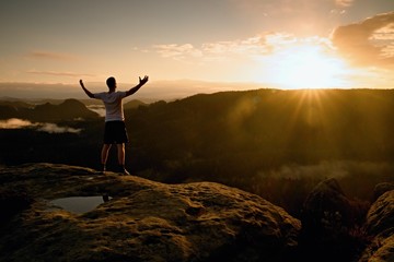 Runner on the peak. Man in his target gesture triumph with hands in the air. Crazy man in black pants and white cotton t-shirt, - 96798069