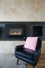 Black leather armchair and pink cushion next to fireplace
