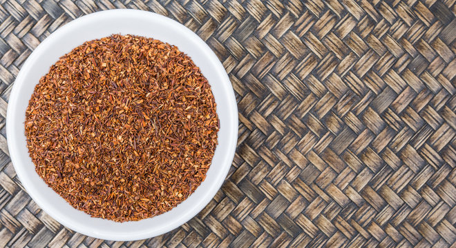 Dried South African rooibos herbal tea in white bowl over wicker background