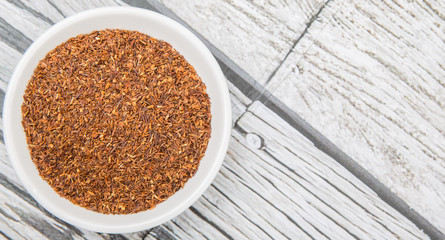 Dried South African rooibos herbal tea in white bowl over wooden background