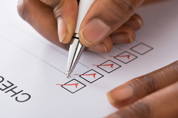 Person's Hand Marking On Checklist Form With Red Pen