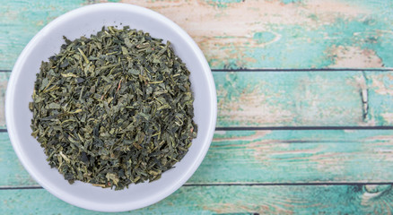 Dried Japanese green tea leaves in white bowl over wooden background