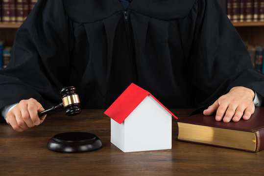 Judge With House Model Hitting Gavel At Desk