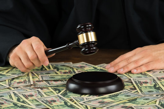 Corrupt Judge Hitting Gavel With Banknotes Spread At Desk