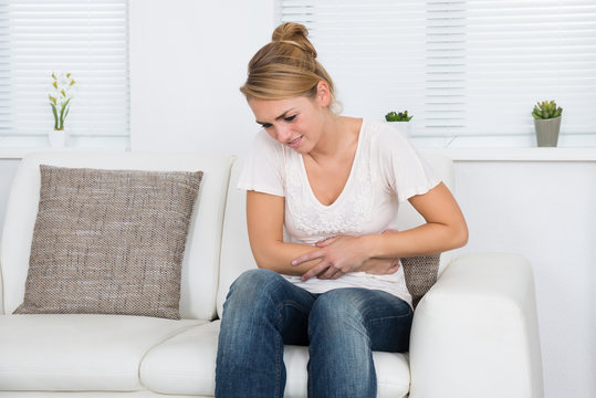 Woman Suffering From Stomach Ache While Sitting On Sofa