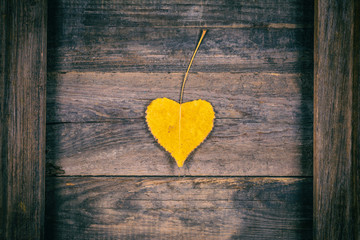 Autumn yellow leaf in the shape of a heart on a wooden background