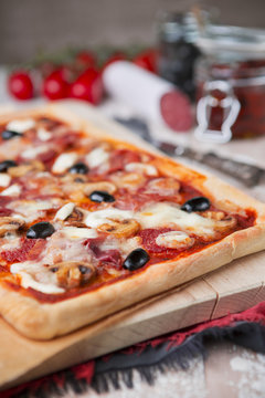 Homemade rectangular pizza on a rustic table with ingredients