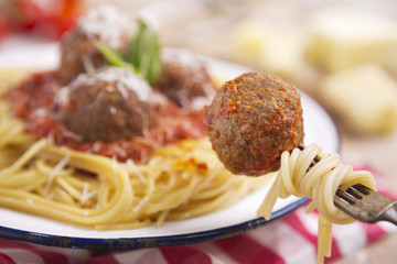 Spaghetti and meatball on a fork, plate in the background
