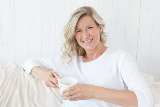 beautiful adult woman with blond hair, smiling, happy drinking coffee, tea.He is sitting on the sofa with a cup in hand. 