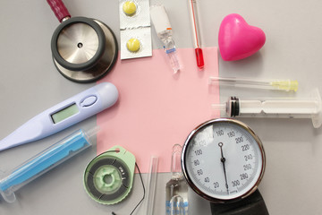 Medical theme -pill, syringe, needle, medical thermometer, heart, blood pressure equipment, surgical thread and stethoscope - copy space on grey background